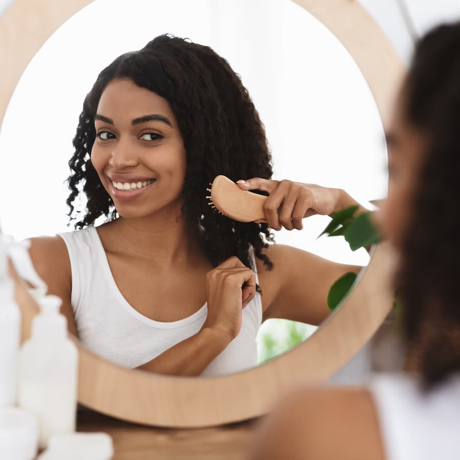 Smiling woman combing her beautiful curly hair near mirror in bathroom
